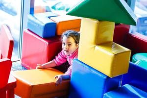 fille jouant sur l'aire de jeux couverte sur le trampoline avec des cubes multicolores en mousse souple. la notion d'enfance. photo