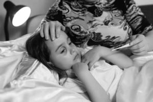 jeune mère vérifiant la température de sa fille malade au lit photo