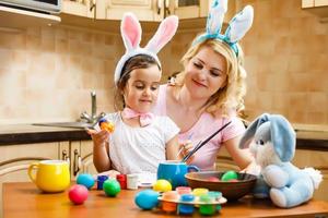 fille et mère en costume de lapin se préparent pour pâques et peignent des œufs photo