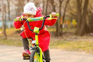 enfant à vélo. enfant à vélo dans un parc ensoleillé. petite fille profitant d'une balade à vélo pour se rendre à l'école par une chaude journée d'été. enfant d'âge préscolaire apprenant à s'équilibrer à vélo dans un casque sûr. sport pour les enfants. photo