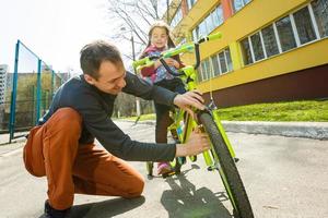 le père a aidé la fille à faire du vélo. faire du vélo dans la rue. concept de mode de vie sain photo