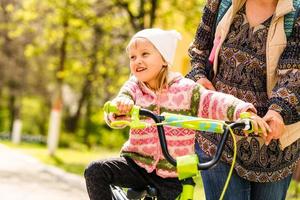 belle et heureuse jeune mère apprenant à sa fille à faire du vélo. à la fois en souriant et en se regardant. parc d'été en arrière-plan. photo