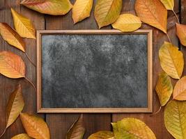 tableau de craie en bois vide sur fond de bois marron et feuilles de cerisier jaunes photo