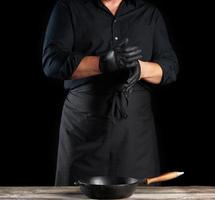 le chef en chemise noire et tablier met des gants en latex noir sur ses mains avant de préparer la nourriture photo