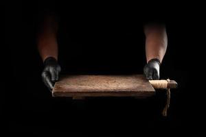 les mains des hommes dans des gants en latex noir tiennent une planche à découper en bois marron vintage vide photo