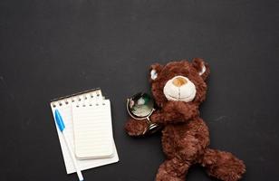 pile de cahiers avec des feuilles blanches vierges et un ours en peluche brun tenant un globe de verre photo