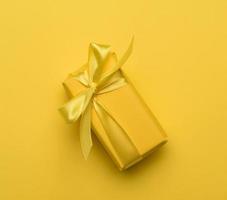 boîte rectangulaire avec un cadeau emballé dans du papier jaune et attaché avec un ruban de soie jaune photo