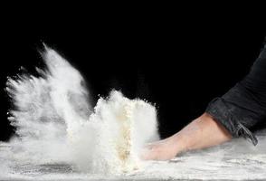 le chef en uniforme noir saupoudre de la farine de blé blanc dans différentes directions, le produit disperse la poussière photo