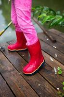 bottes en caoutchouc rouges pour enfants sur la jetée au bord du lac après la pluie. enfance heureuse.