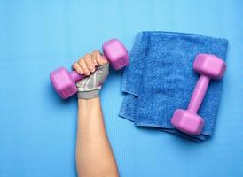 la main féminine dans un gant de sport rose tient un haltère violet d'un kilogramme photo