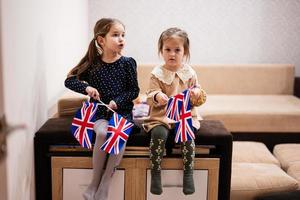 deux sœurs sont assises sur un canapé à la maison avec des drapeaux britanniques sur les mains. grande-bretagne enfants filles avec drapeau. photo