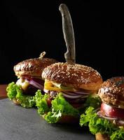 délicieux burgers avec escalope de bœuf frite, tomate, laitue et oignons, pain croustillant à la farine de blé blanc aux graines de sésame photo