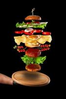 planche de bois ronde et couches d'un grand cheeseburger flottant dans l'air photo