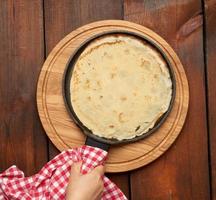 grande crêpe ronde cuite dans une poêle à frire noire sur une table en bois marron photo