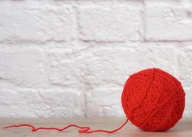 Boule rouge avec fil de laine sur fond de mur de briques blanches photo