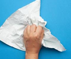 femme tient dans sa main une feuille de papier froissée dans une cage sur fond bleu, photo