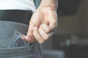 jeune homme jeans poche arrière pour transporter des préservatifs prenant dans la main le préservatif d'un jean, le concept de rapports sexuels protégés sur le lit prévient l'infection. photo