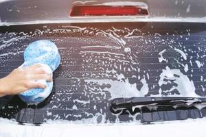 personnes travailleur homme tenant la main éponge bleue et fenêtre nettoyante en mousse à bulles pour laver la voiture. concept de lavage de voiture propre. laisser de la place pour écrire des messages. photo