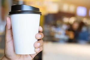 jeune femme main tenant une tasse de papier à emporter, boire du café chaud sur la table en bois dans le café-café. photo