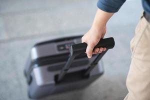 homme d'affaires marchant à l'extérieur du bâtiment des transports publics avec des bagages aux heures de pointe. voyageur d'affaires tirant une valise dans un terminal d'aéroport moderne. bagages voyage d'affaires. photo