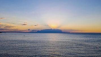 image du lever du soleil sur la mer caché par des nuages aux couleurs intenses et des rayons de soleil photo