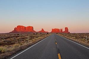 Une route droite mène directement au rouge dans le soleil du soir formation rocheuse dans le parc national de Monument dans l'Utah photo