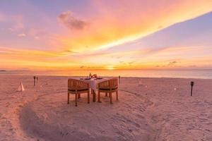 configuration de la table pour la cérémonie de mariage sur la plage au coucher du soleil. dîner de destination romantique, célébration romantique d'anniversaire de couple. arrangement d'amour dîner ensemble sur la côte de l'île. vue imprenable sur la mer du ciel photo