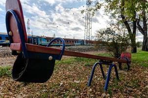 balançoires vides sur une aire de jeux vide sans personnes sur fond de trains brûlés en ukraine photo