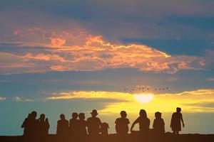 silhouette personnes assises sur le sol et coucher de soleil sur le ciel coloré nuage orange et oiseaux volant photo