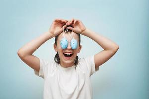 jeune garçon souriant tenant des oeufs de pâques dans sa main et couvrant ses yeux avec sur un fond bleu photo