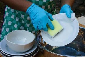 les mains utilisent un épurateur éponge pour nettoyer le plat. concept, corvée quotidienne, ustensiles de cuisine de nettoyage domestique. porter des gants de protection pour se protéger les mains des allergies aux substances chimiques. photo