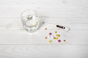 pilules avec thermomètre et verre d'eau sur une table en bois blanche. notion médicale photo