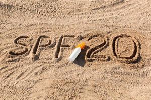 facteur de protection solaire vingt. SPF 20 mot écrit sur le sable et bouteille blanche avec crème solaire. fond de concept de soins de la peau photo