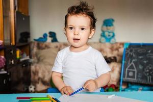 un petit garçon dessine sur des feuilles de papier posées sur la table avec des crayons de couleur photo