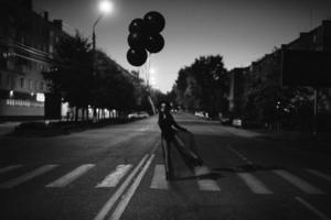 une fille en noir avec des ballons noirs dans ses mains pose debout sur la route photo