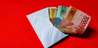 roupie indonésienne dans une enveloppe blanche isolée sur fond rouge. le concept de donner angpao le nouvel an chinois photo
