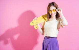 photo d'une adolescente asiatique avec planche à roulettes sur fond rose