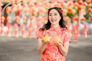 joyeux Nouvel An chinois. belle femme asiatique vêtue d'une robe traditionnelle cheongsam qipao tenant de l'argent en or ancien et de l'orange fraîche dans un temple bouddhiste chinois. célébrer le nouvel an lunaire chinois. photo