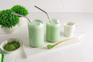 deux tasses sous forme de canette de bière avec du thé matcha latte fraîchement préparé sur une planche en céramique blanche en face du mur de briques et des plantes dans des pots de fleurs. photo