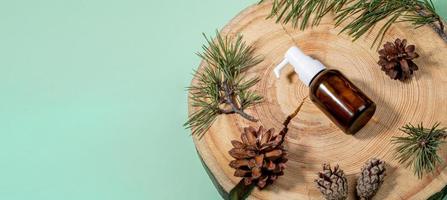 bannière avec petite bouteille en verre à l'huile essentielle de pin, branches, cônes sur scie en bois coupée sur fond vert menthe. photo