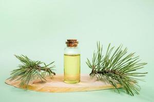 une petite bouteille en verre avec de l'huile essentielle de pin sur une scie à bois coupée sur du vert menthe. photo