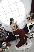portrait d'une jolie jeune fille confortable s'asseoir et boire du vin, porter une robe rouge dans un salon de noël décoré à l'intérieur photo