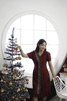 portrait d'une jolie jeune fille vêtue d'une robe rouge, souriant à la caméra, debout dans un salon de noël décoré à l'intérieur photo