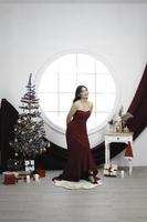 portrait d'une jolie jeune fille vêtue d'une robe rouge, souriant à la caméra, debout dans un salon de noël décoré à l'intérieur photo