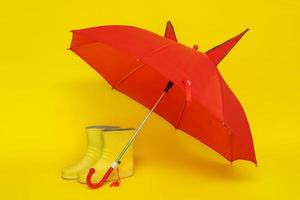 bottes en caoutchouc jaunes pour enfants sous un parapluie rouge pour enfants sur fond jaune photo