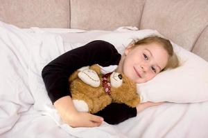 petite fille se trouve dans son lit avec un ours en peluche et sourit photo