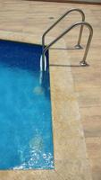 coin d'une piscine avec bordure en marbre et murs en céramique bleue et échelle de piscine photo