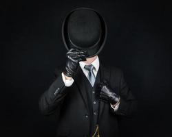portrait d'un gentleman anglais en costume sombre et gants en cuir basculant le chapeau melon en guise de salutation. majordome britannique classique ou homme d'affaires. photo