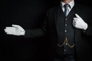 portrait de majordome en costume sombre et gants blancs debout avec un geste de bienvenue. concept de l'industrie des services et de l'hospitalité professionnelle photo