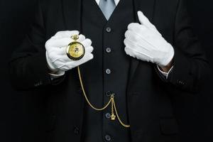 portrait de majordome en costume noir et gants blancs tenant une montre de poche en or. concept d'industrie de services et d'hospitalité professionnelle. photo